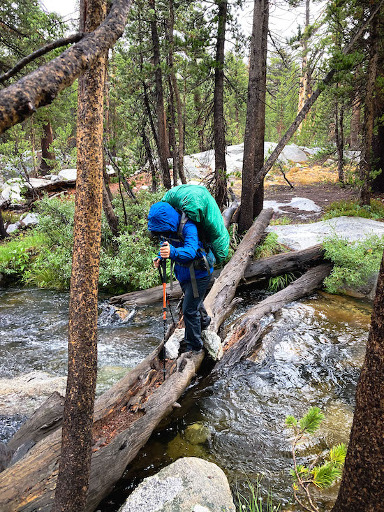 Sam Stych crossing a creek on a log in the Sierras